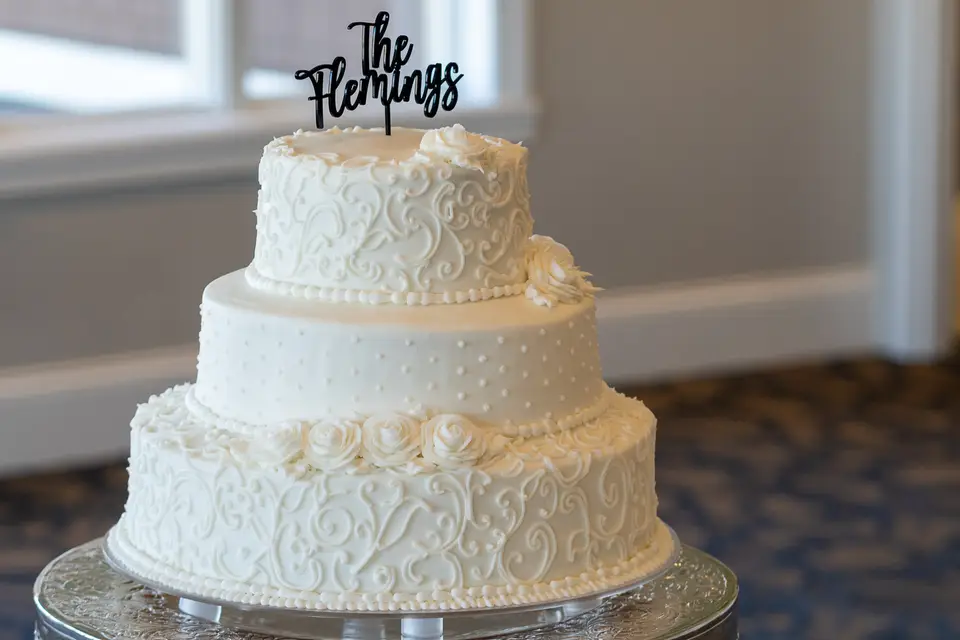 Three-tier white wedding cake with piped scrollwork details and a custom topper by Taylor's Bakery